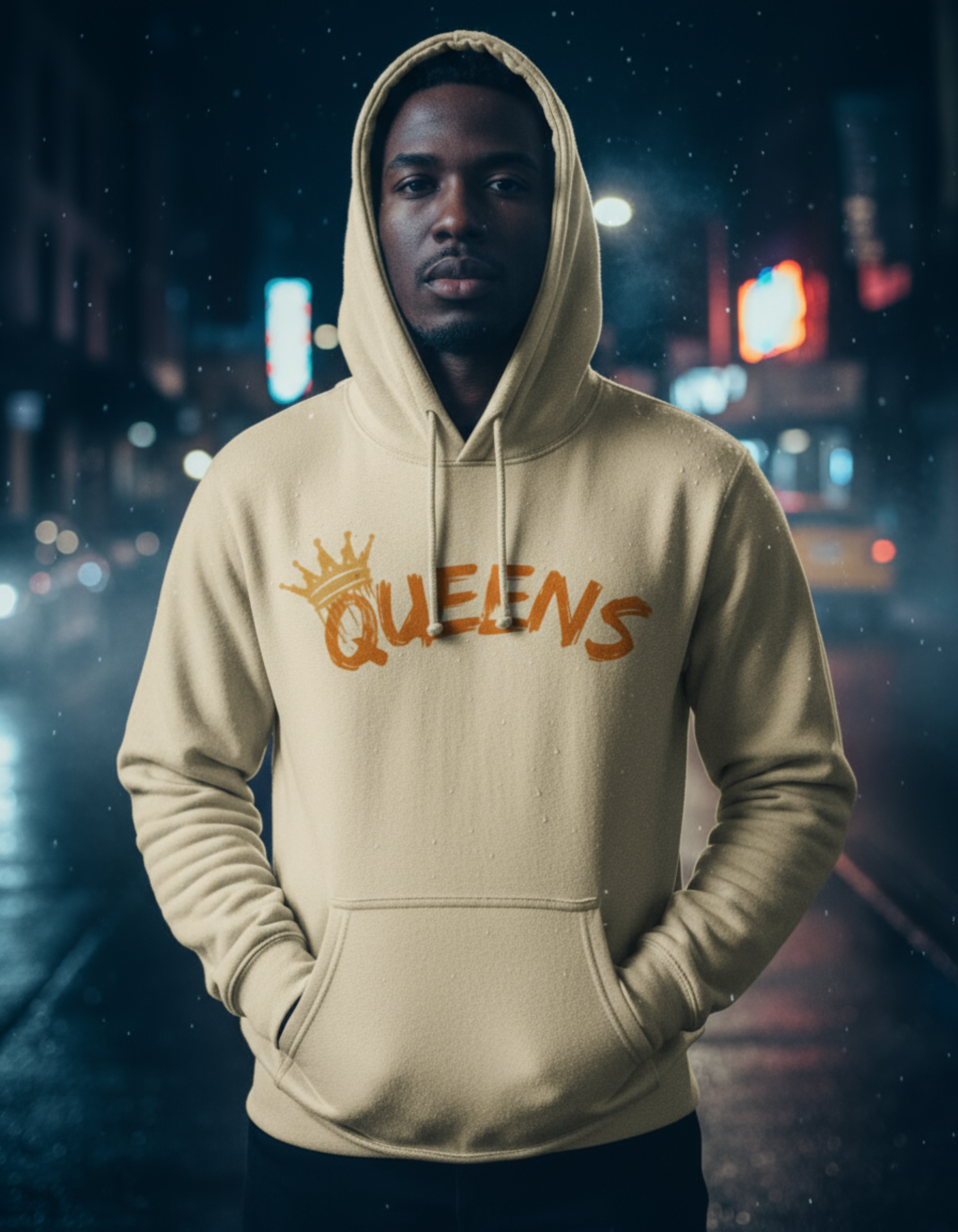Man wearing a beige hoodie with 'QUEENS' printed on it against a blurred city street background.