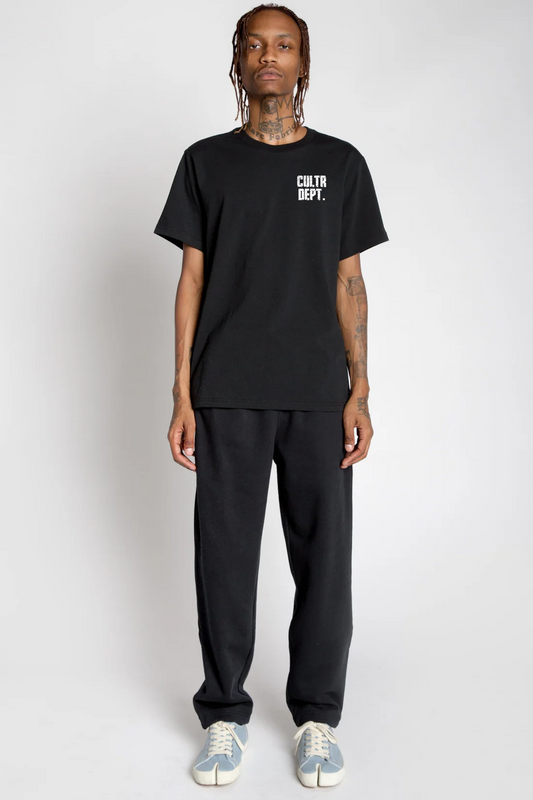 Person wearing a black t-shirt with text "CULTR DEPT." and black pants on a white background