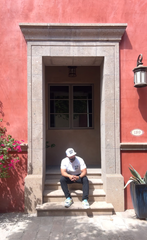 Person sitting on a stone step in front of a red building with a white door.