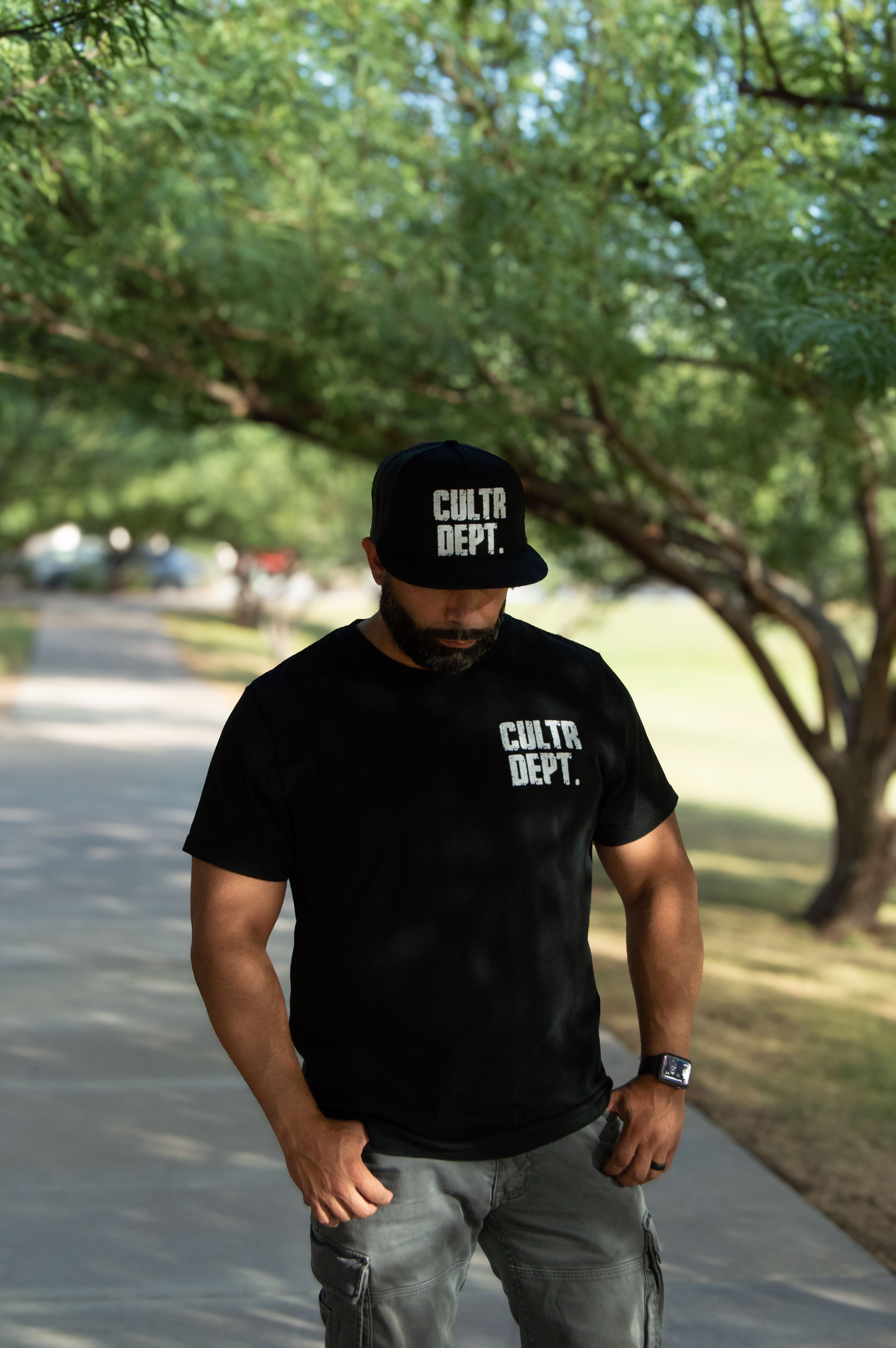 Man wearing a black 'Cultur Dept.' t-shirt and cap outdoors.